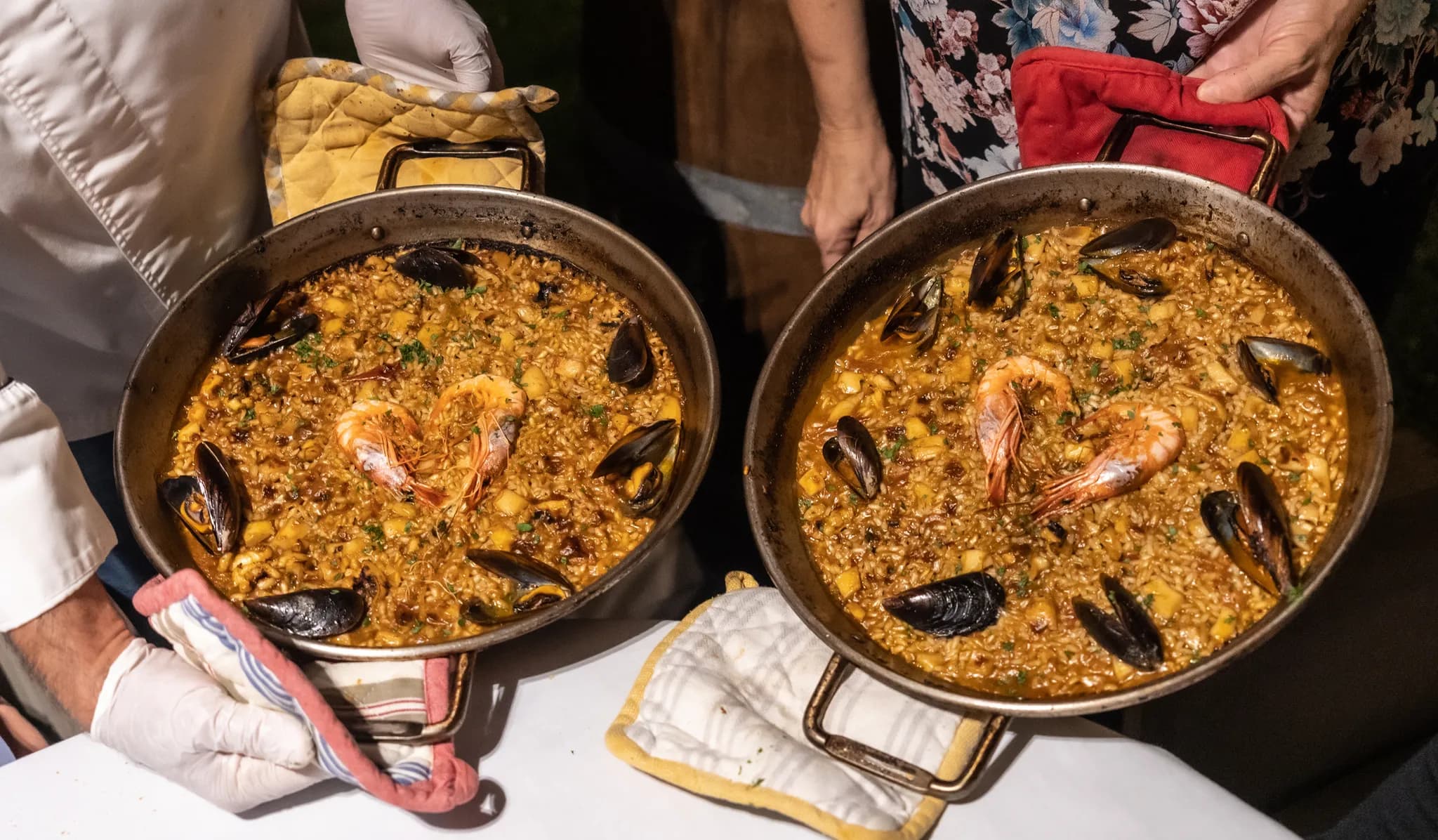 Dois cozinheiros seguram duas paellas de marisco acabadas de fazer nas respetivas frigideiras