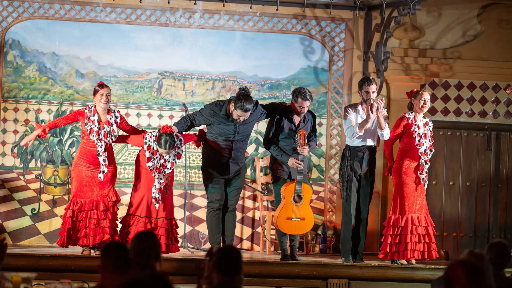 Bailarinas de flamenco com vestidos vermelhos de folhos e músicos a agradecer ao público no final de um espetáculo