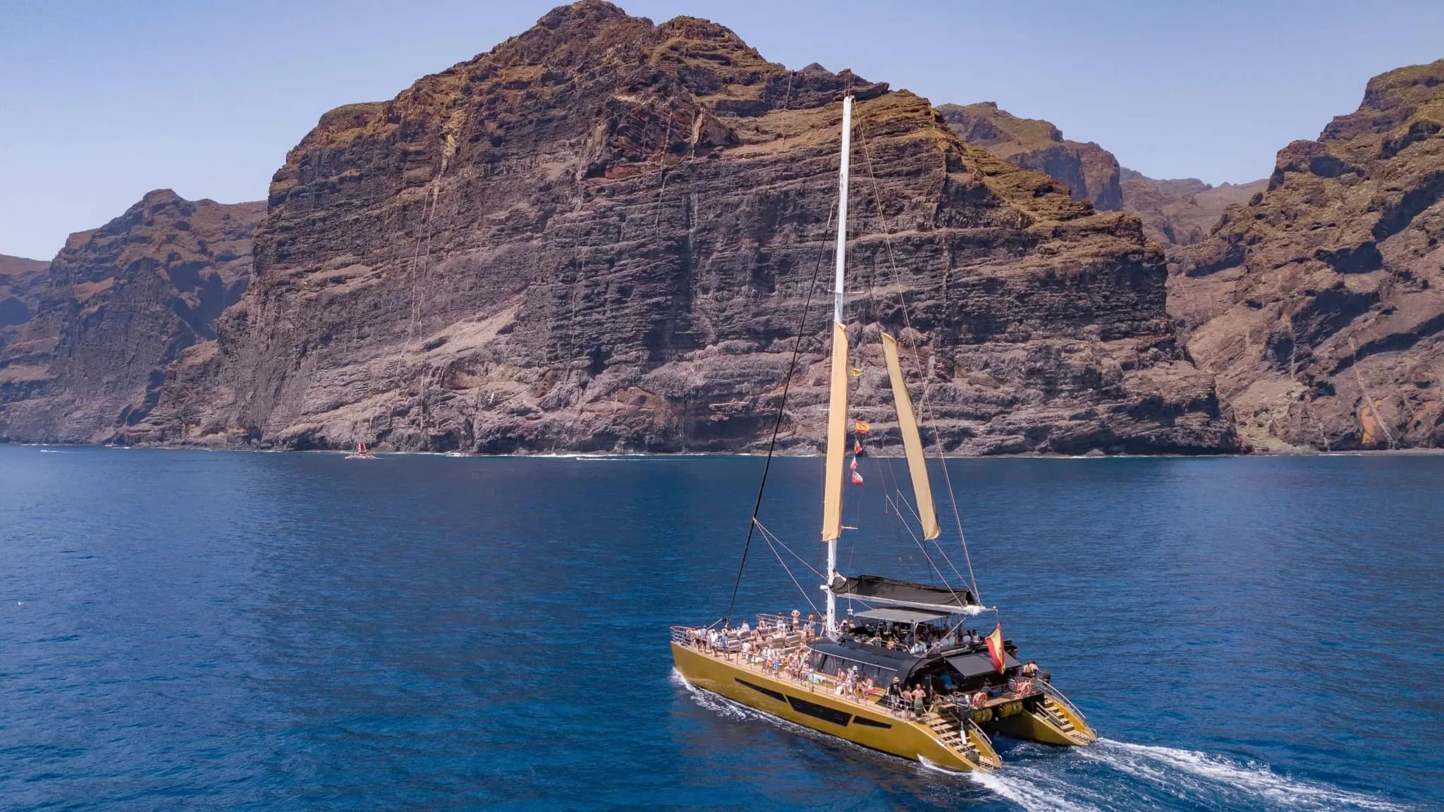 Um catamarã cheio de convidados a navegar junto a imponentes falésias